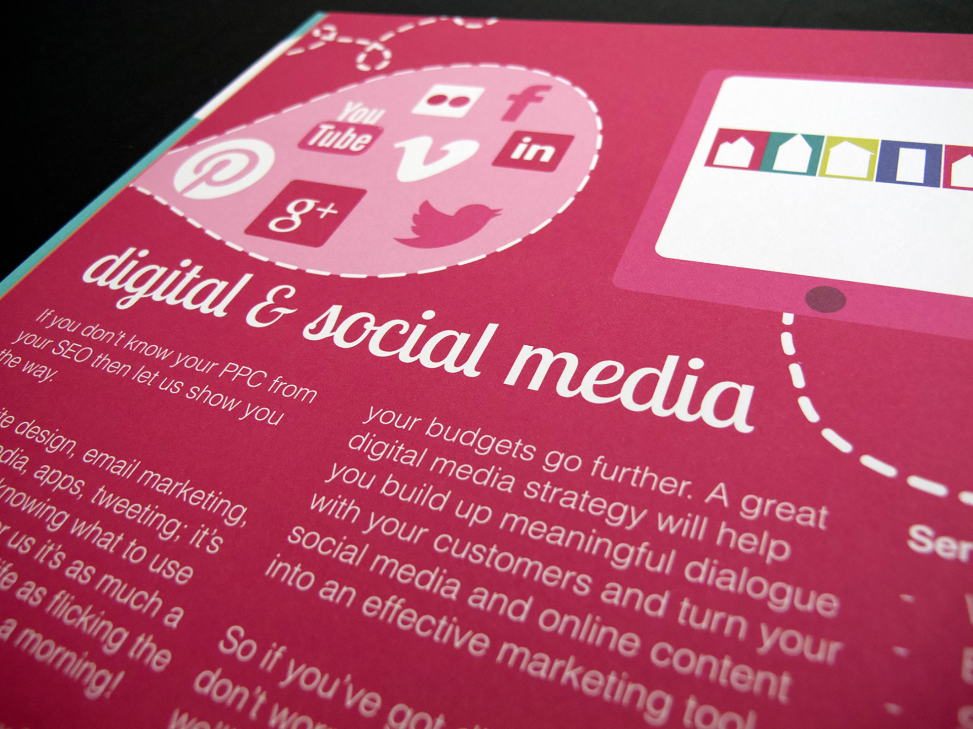 A close-up, angled photo of the digital and social media brochure page. The page is a bold pink colour with white text. Social media icons appear in a speech bubble, and there is an illustration of a tablet device. 