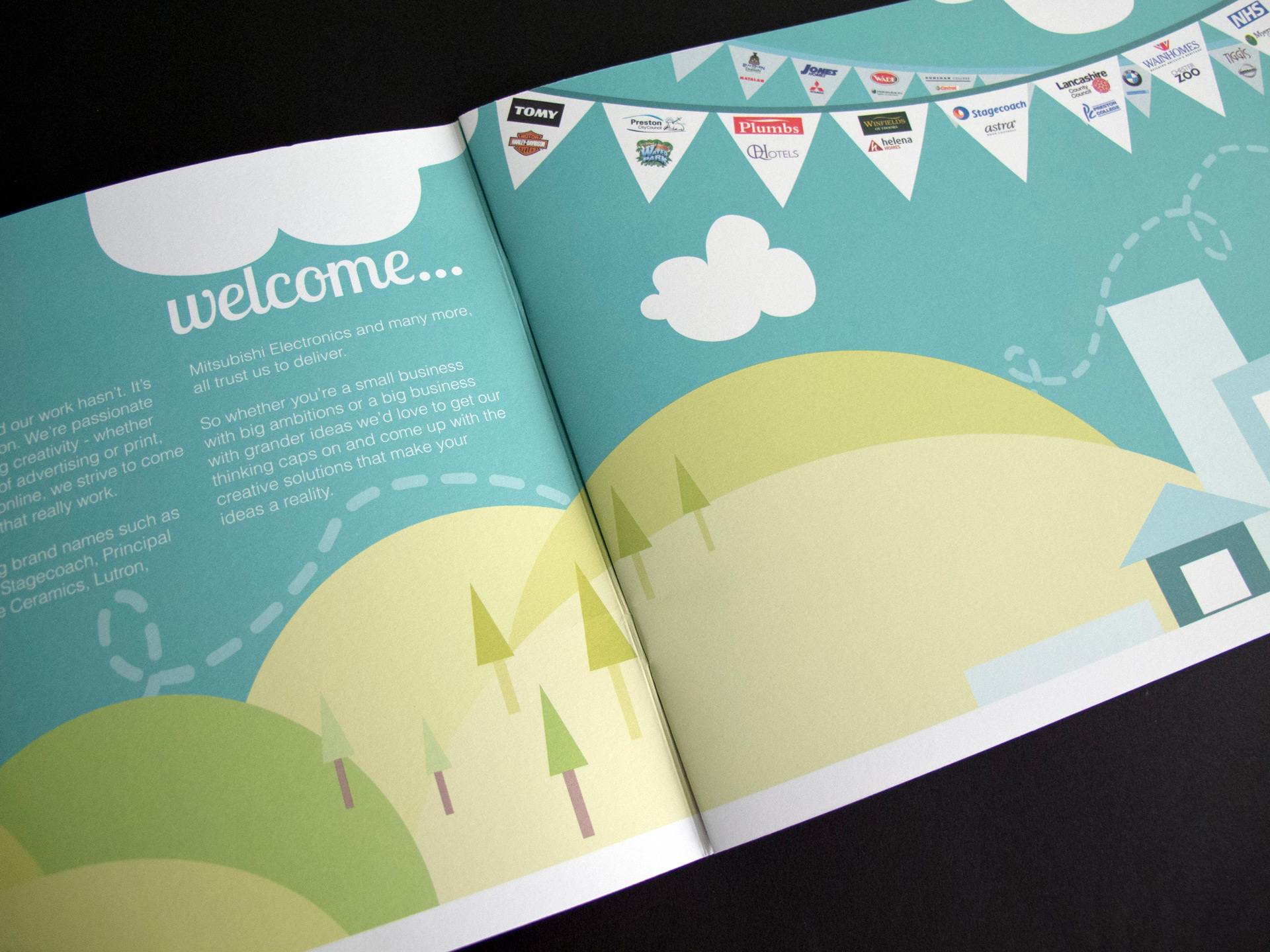 Photo of the brochure welcome pages that are in a vector illustration style. There are green hills with trees and a blue sky that span both pages. On the right page, the sky is filled with bunting depicting Heckford's client logos. 