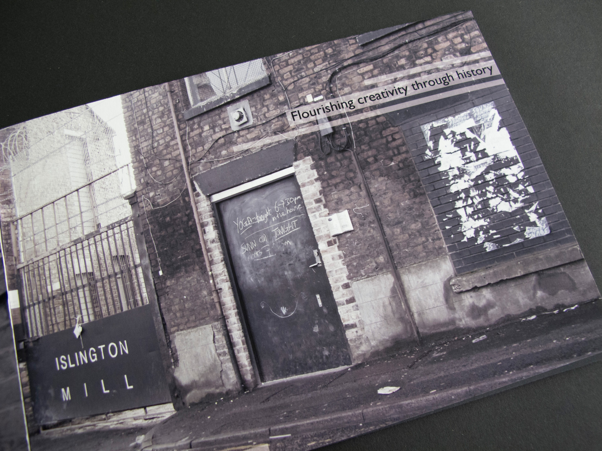 This booklet page features a desaturated photograph of a mill in Salford. The building in the photo has a bricked-up window and there is a gate to the left of it with a sign that reads 'Islington Mill'. Overlaid on the photograph are the words 'Flourishing creativity through history'.