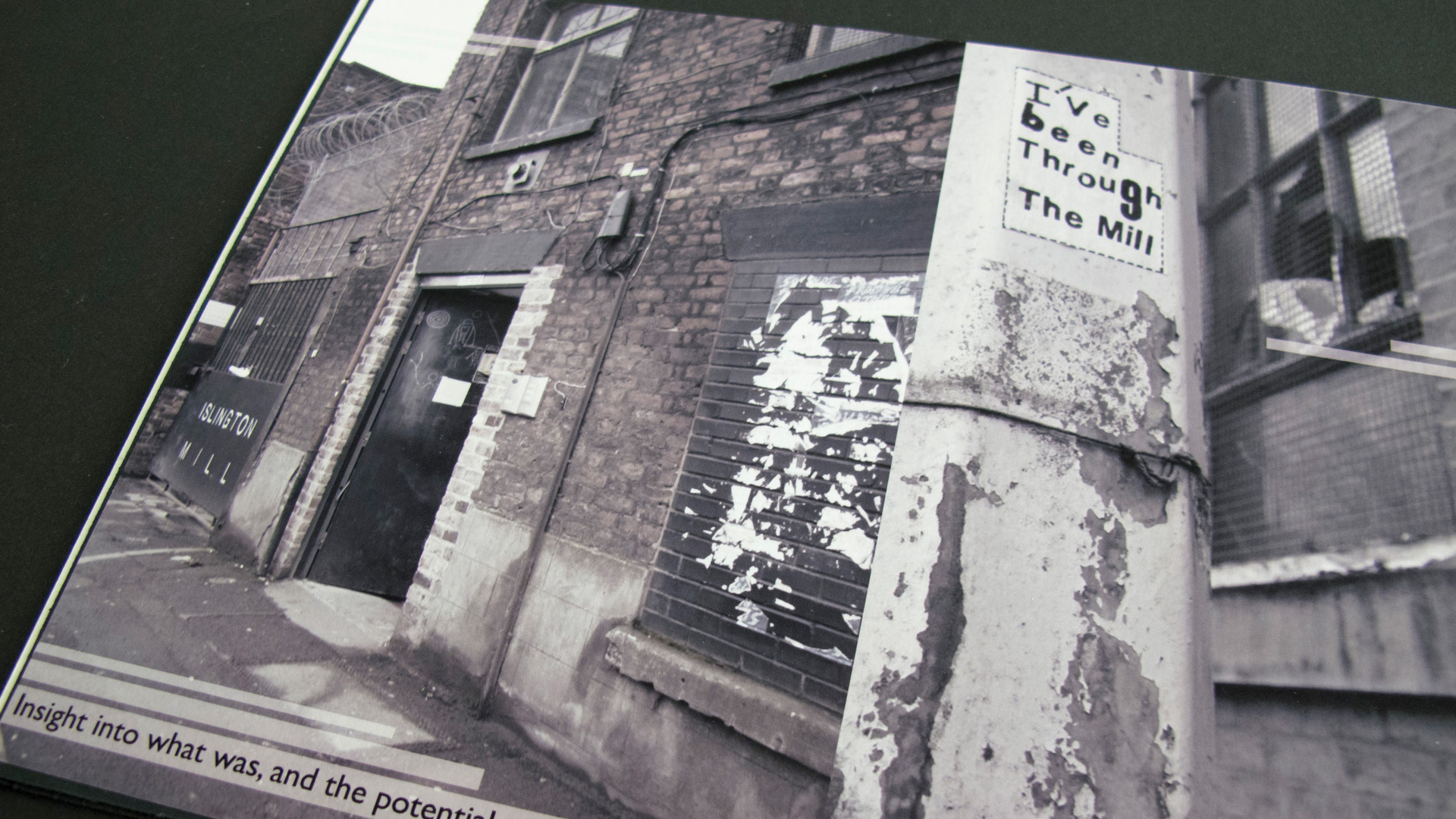 A desaturated photograph of a mill in Salford. A lamppost is in the foreground, with a sticker stating 'I've been through the mill'